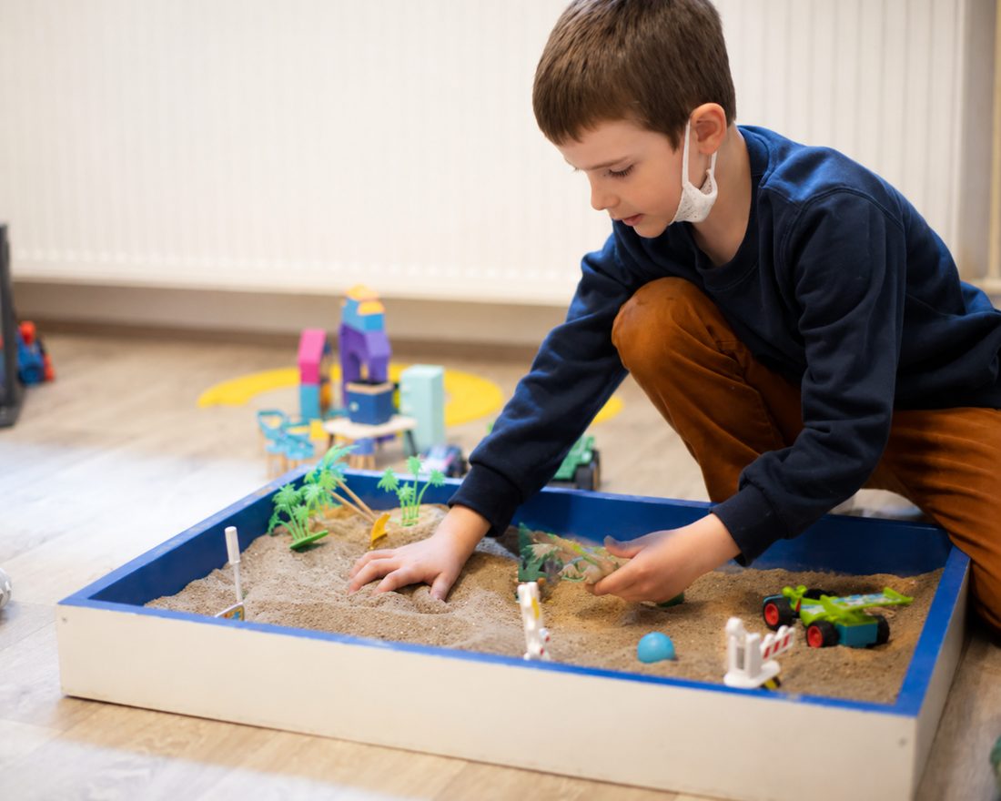 A child arranging small figures in a sand tray